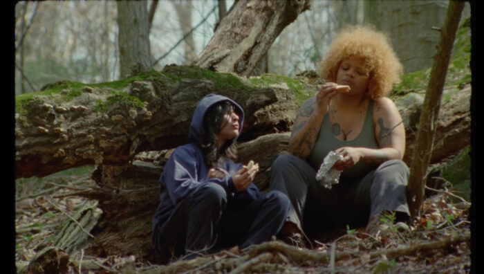 Two young women sitting and eating in a forest.