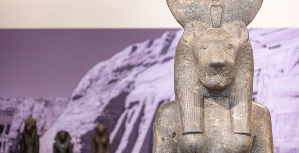 Statue of an Egyptian god with an image of the pyramids on the wall behind