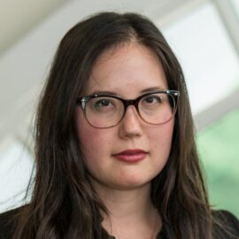 Color photograph of a woman with long, brown hair and eyeglasses