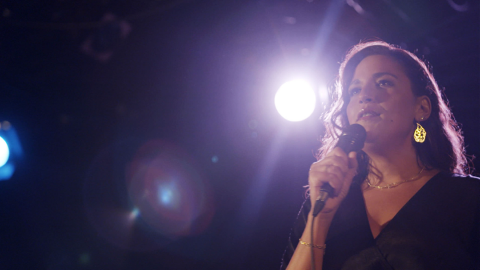 A woman holding a microphone with a spotlight behind her.